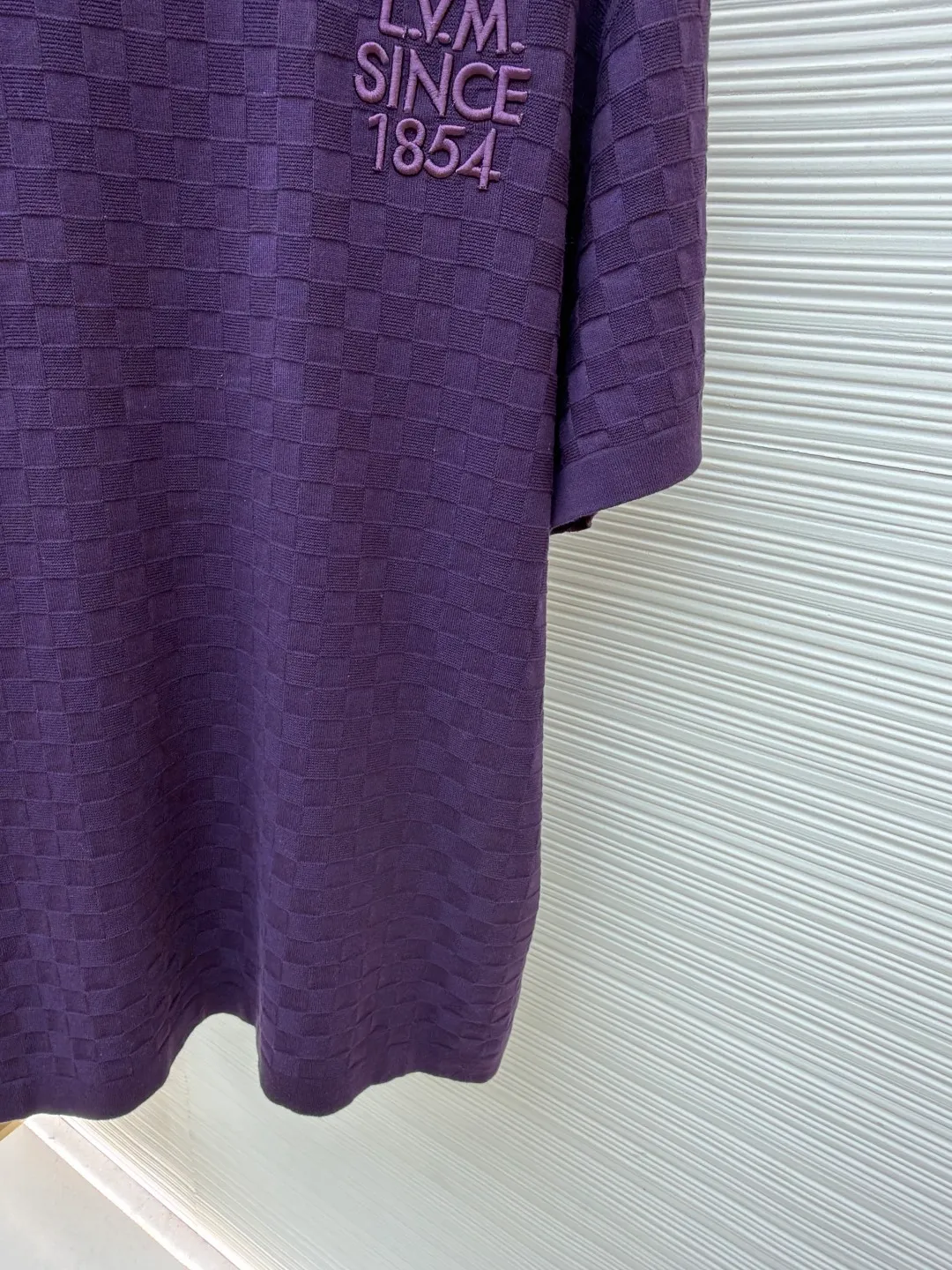 LOUIS VUITTON letter embroidered dark checkerboard jacquard short sleeves ●Original version: Purchased and developed at 9350 ●Item number: 1682319-B00 ●Fabric: 100% cotton ●Technology: jacquard knitting ●Color: Purple ●Version: Fitted version ●Weight: about 340 grams ●Size: S-M-L-XL ●Description: This Louis Vuitton purple knitted short-sleeve is made of custom worsted wool blended fabric. It is created with an 18-needle high-density weaving process using a computerized flat knitting machine to create a three-dimensional checkerboard texture. The checkered pattern is laser positioned and patterned. The size and spacing of each grid are accurate to 0.1 cm, showing a regular relief texture. The left chest uses same-color inlay embroidery technology, and the "LVM SINCE 1854" logo is embroidered with a high density of 1200 stitches/square centimeter. The embroidery thread is made of high-elastic mercerized cotton thread of the same color as the body, forming a natural texture layer with the knitted base. The neckline adopts seamless cylindrical rib technology, which is not easy to loose after high-temperature shaping treatment. The shoulders are made of seamless bonding technology to reduce the abruptness of the seams. The overall micro-profile tailoring combined with the invisible stitching technology of the side seams not only ensures the comfort of wearing, but also makes the body lines smoother. Each process has undergone multiple quality control tests by the brand to ensure the quality and durability of the craftsmanship. The overall wiring is straight and delicate, the fabric is comfortable and soft, and the color is consistent without color difference. It can be matched with the same style to create a fashionable look and control various occasions. Customized accessories, complete with three standards, same style for men and women!